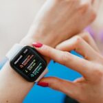 Unrecognizable female with manicure checking smartwatch on hand while sitting on yoga mat